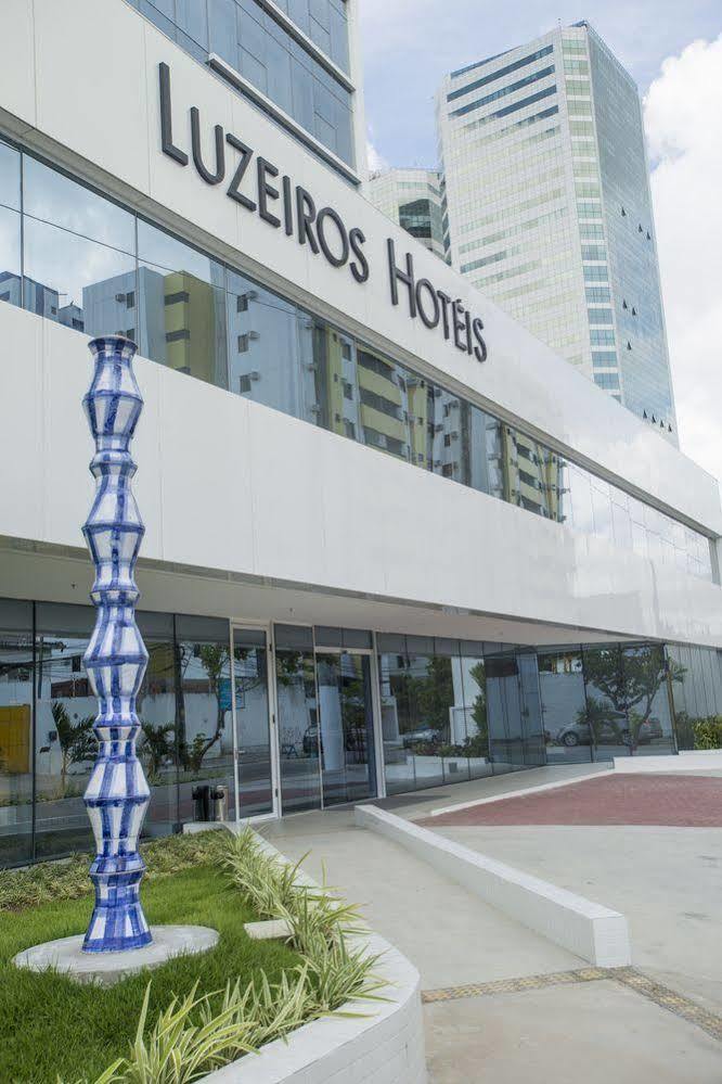 Hotel Luzeiros Recife Exteriör bild The photo shows a modern hotel building with large glass windows and a sleek, white facade. In front of the hotel, there is a tall, decorative sculpture that features a unique, twisting shape with a blue and white color scheme. The hotel name is prom